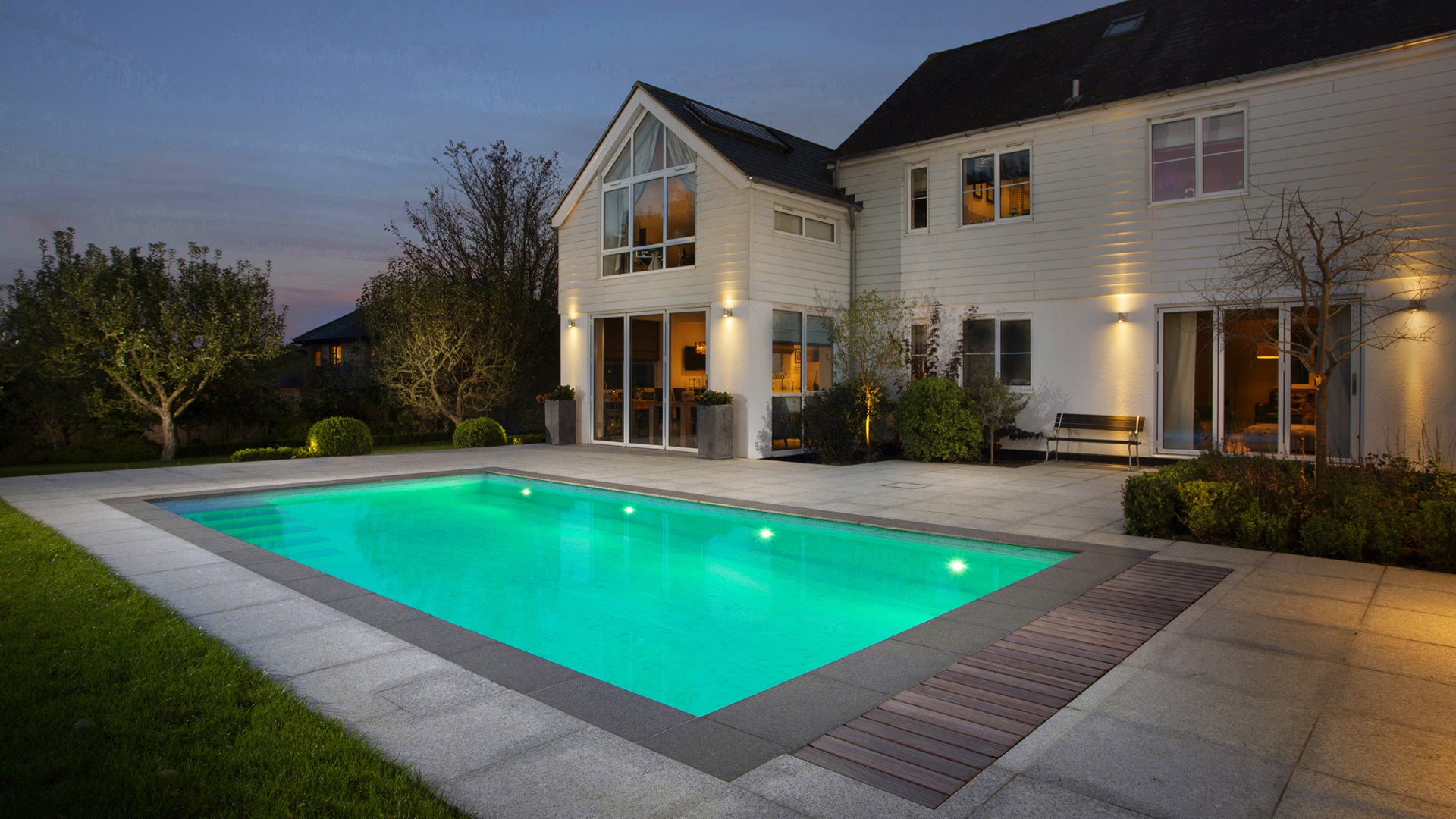 A photo of a beautiful large house with swimming pool. Stone surround. evening light. 